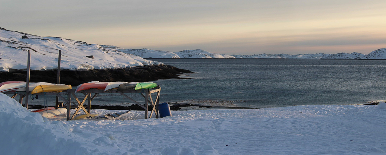 Billedet viser kajakker på bredden med fjord i baggrunden